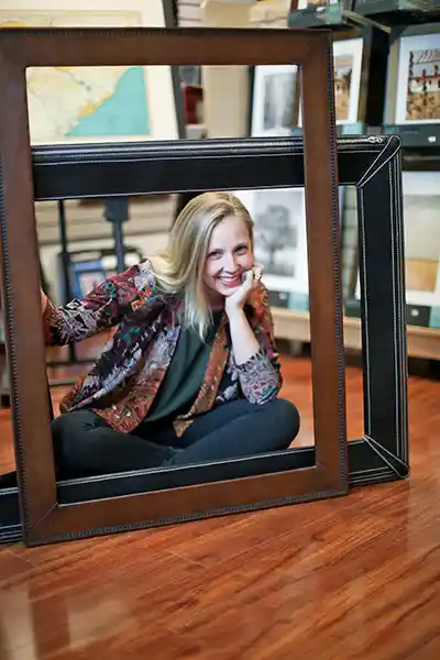 Lauren Owens in the Frames Unlimited store smiling as she holds 2 picture frames.