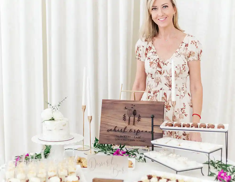 Whisk & Spoon owner/baker Debbie Gardiner stands in front of a table loaded with her baked treats.