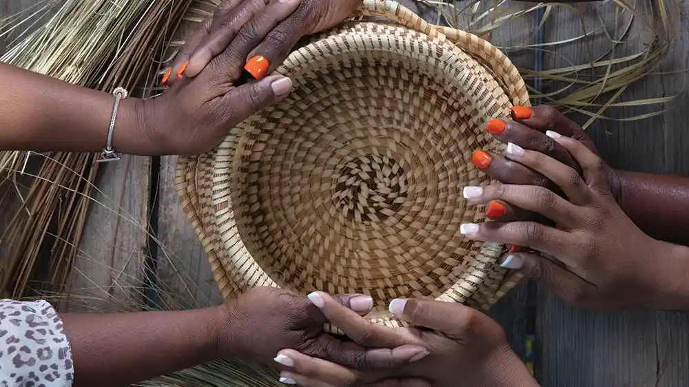 A sweetgrass basket with 3 generations worth of weaver's hands holding it.