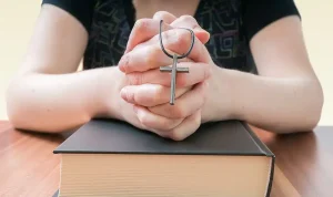 A young woman holding a cross as she prays.