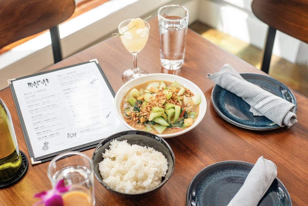 A mouth watering table of Makan's Malaysian-inspired cuisine showing their menu, plates of food and some beverages.