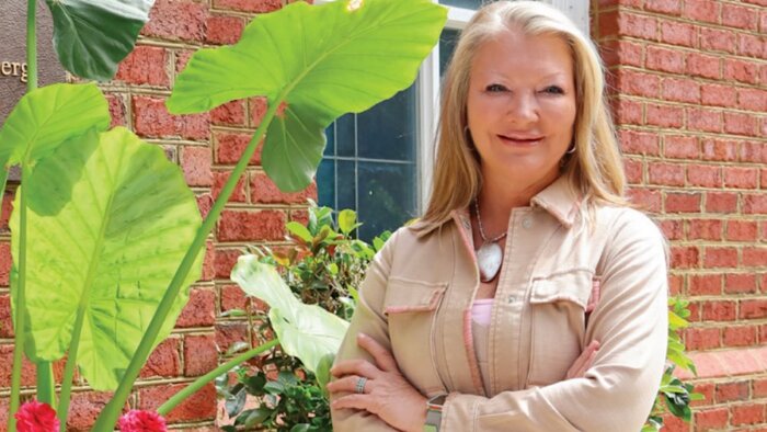 Dina Mewett of BeWell@Home standing outside next to a plant