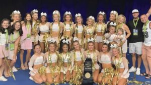This image displays Pack Athletics Cheerleading team Miss 6 with a trophy after winning the Cheerleading Worlds