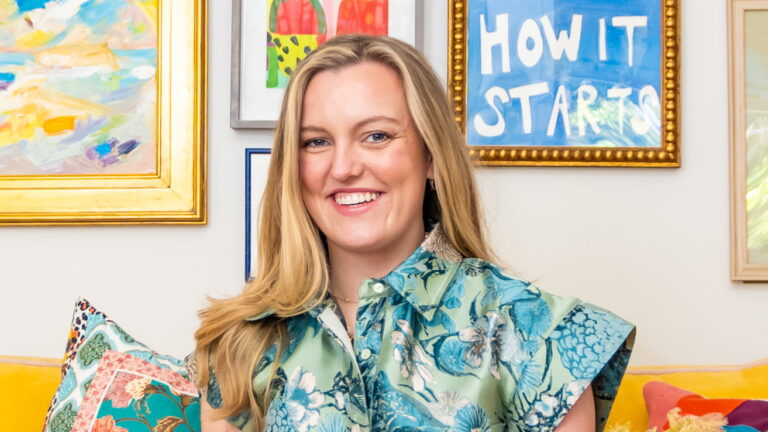 This image displays a woman in her living room in front of a collage of pictures. She is in a blue and green floral button-up short sleeve dress.